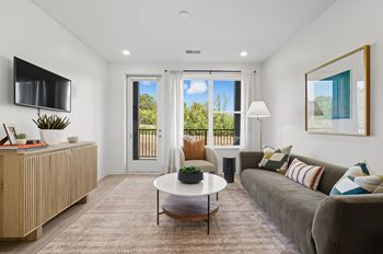 A living room with a grey couch, a white coffee table, and a flat screen TV mounted on the wall.